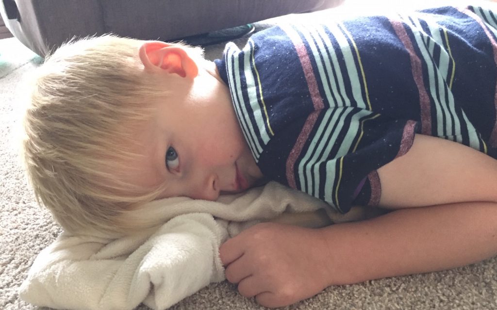preschool boy laying on the carpet with a blanket peeking at the camera out of the corner of his eye